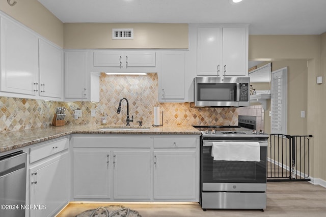 kitchen with light stone countertops, sink, stainless steel appliances, white cabinets, and light hardwood / wood-style flooring