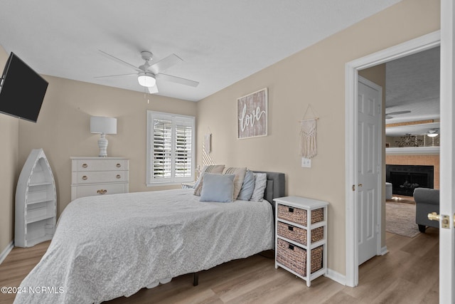 bedroom featuring ceiling fan, light wood finished floors, a fireplace, and baseboards