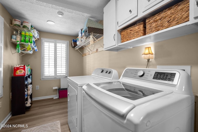 clothes washing area featuring washer and clothes dryer, a textured ceiling, light hardwood / wood-style floors, and cabinets