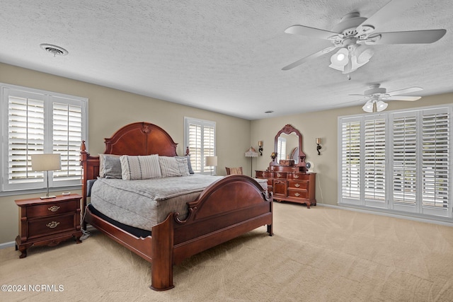 bedroom featuring light colored carpet, visible vents, ceiling fan, a textured ceiling, and baseboards