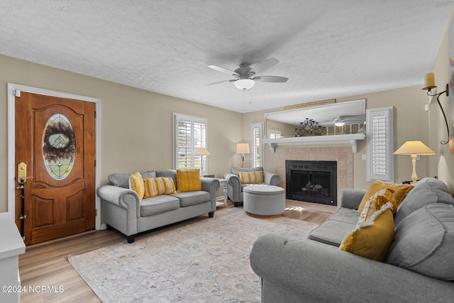 living area with a textured ceiling, a fireplace, a ceiling fan, and wood finished floors