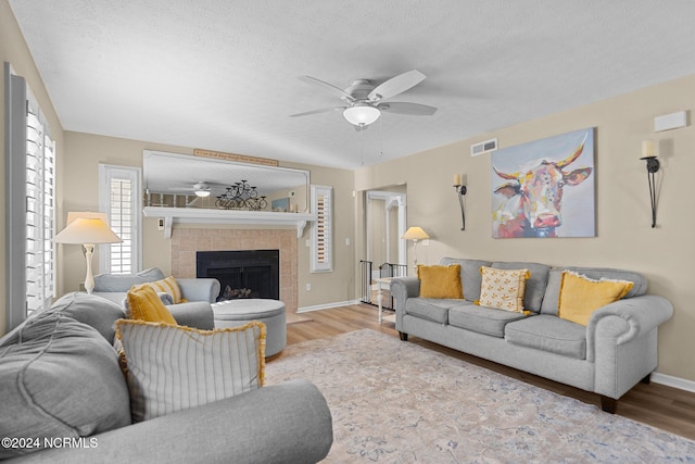 living room featuring a textured ceiling, a fireplace, light wood-type flooring, and ceiling fan