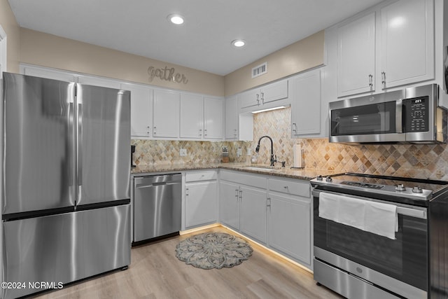 kitchen featuring a sink, light wood-style floors, white cabinets, appliances with stainless steel finishes, and backsplash