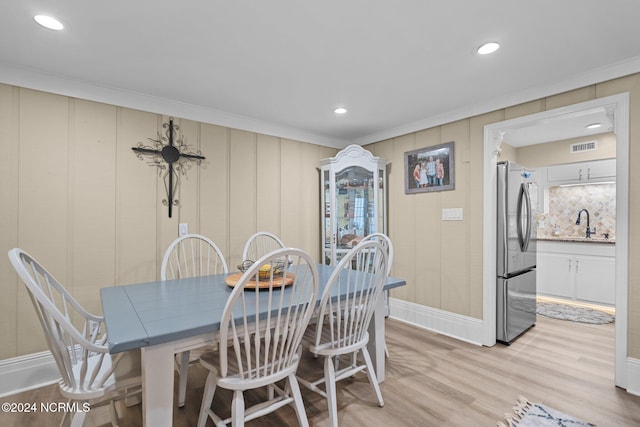 dining space with light hardwood / wood-style floors, wood walls, ornamental molding, and sink