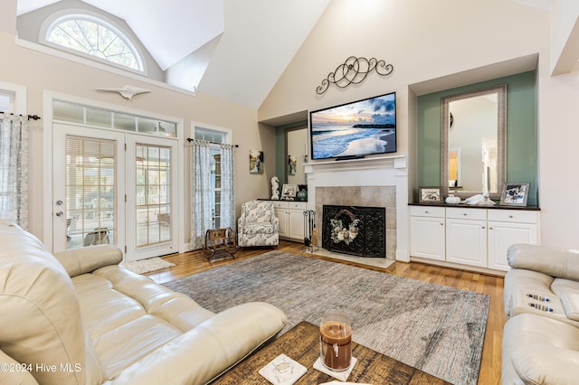 living room featuring a tiled fireplace, light hardwood / wood-style flooring, and high vaulted ceiling