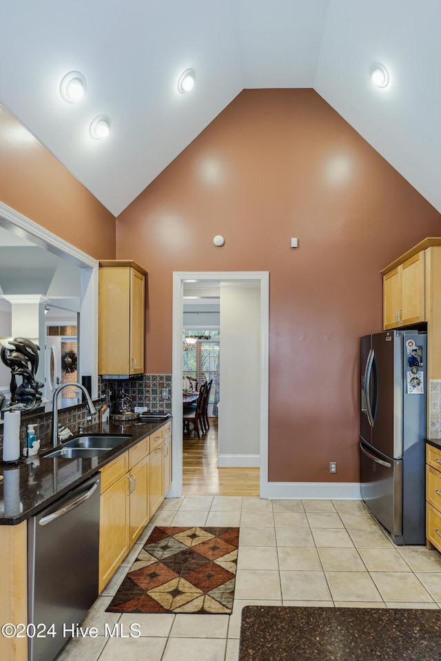 kitchen with appliances with stainless steel finishes, high vaulted ceiling, dark stone counters, and sink