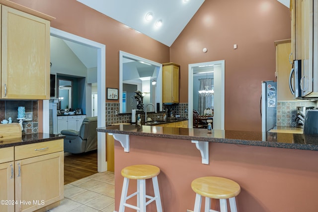 kitchen with light brown cabinets, a kitchen breakfast bar, sink, decorative backsplash, and kitchen peninsula