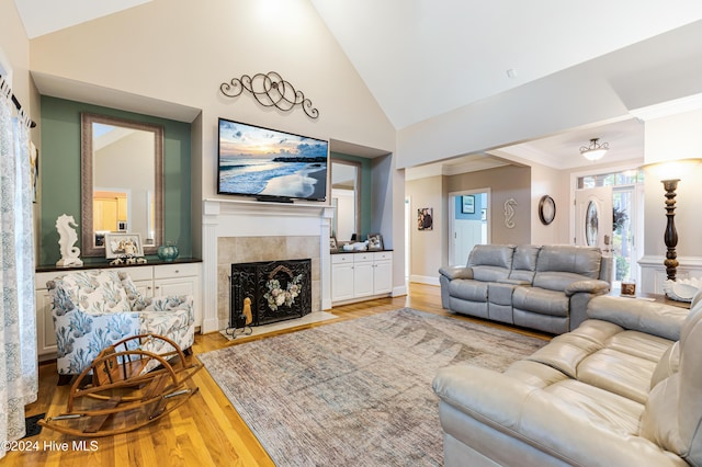 living room with crown molding, a fireplace, high vaulted ceiling, and light hardwood / wood-style flooring