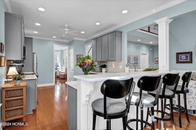 kitchen with a kitchen breakfast bar, light hardwood / wood-style flooring, kitchen peninsula, gray cabinetry, and decorative columns