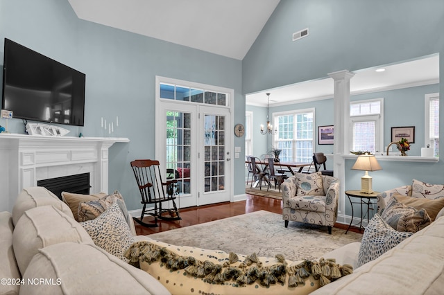 living room with hardwood / wood-style flooring, high vaulted ceiling, decorative columns, a tile fireplace, and a notable chandelier