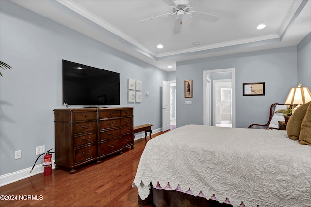 bedroom featuring ceiling fan, connected bathroom, a tray ceiling, wood-type flooring, and ornamental molding