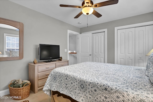 bedroom featuring ceiling fan, light carpet, and multiple closets