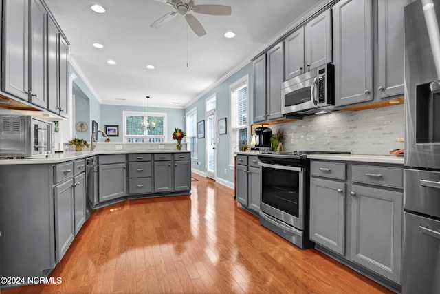 kitchen featuring appliances with stainless steel finishes, light hardwood / wood-style flooring, gray cabinetry, crown molding, and decorative light fixtures