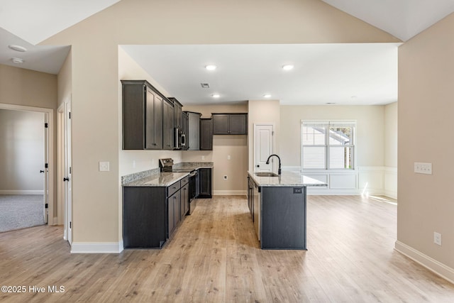 kitchen featuring vaulted ceiling, light stone counters, stainless steel appliances, and a sink