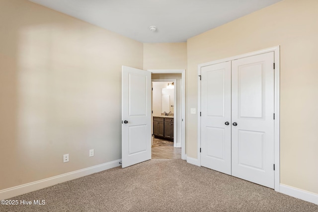 unfurnished bedroom with a closet, light carpet, a sink, and baseboards