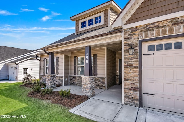 view of exterior entry featuring roof with shingles, a yard, a porch, a garage, and stone siding