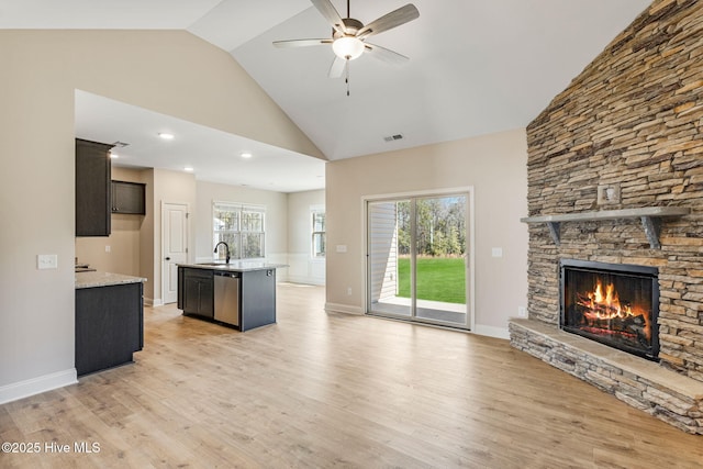 kitchen featuring a fireplace, a sink, open floor plan, light wood-type flooring, and dishwasher