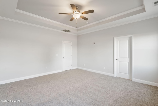 carpeted empty room with ornamental molding, a tray ceiling, visible vents, and baseboards