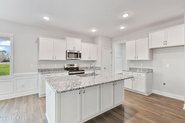 kitchen with white cabinets, a center island with sink, stainless steel appliances, and a sink