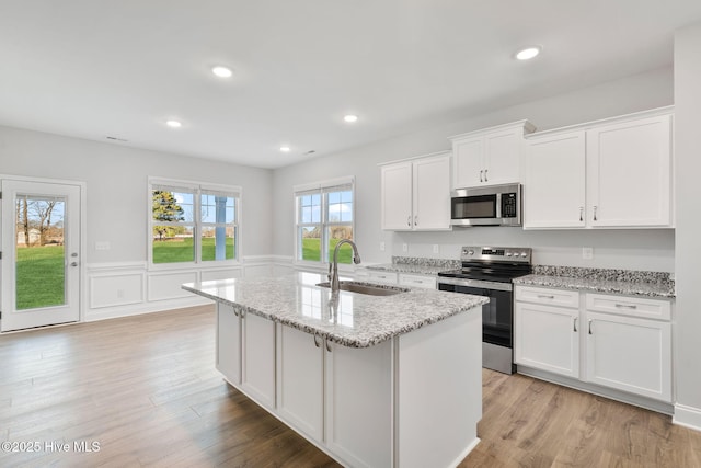 kitchen with appliances with stainless steel finishes, a sink, light wood finished floors, and a center island with sink