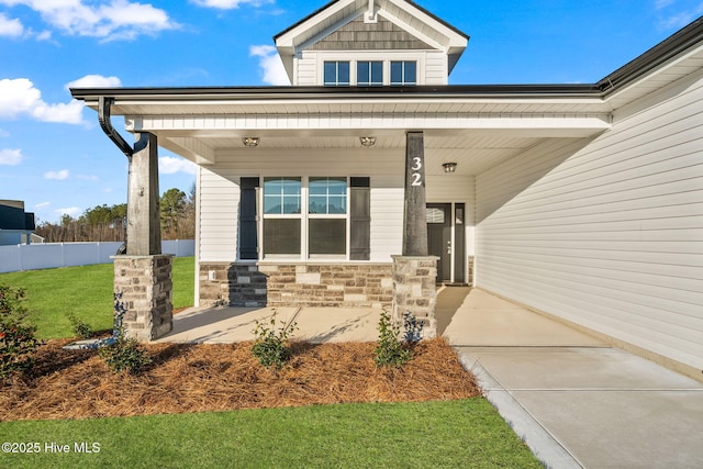 entrance to property with stone siding, covered porch, a lawn, and fence