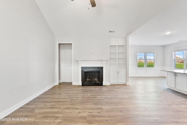 unfurnished living room featuring lofted ceiling, light wood-style flooring, a fireplace with flush hearth, visible vents, and a ceiling fan