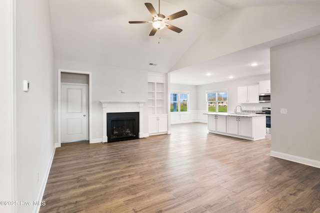 unfurnished living room with a fireplace, wood finished floors, a sink, a ceiling fan, and baseboards