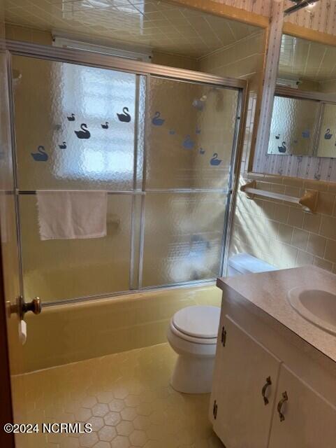 full bathroom featuring tile patterned floors, toilet, vanity, tile walls, and shower / bath combination with glass door