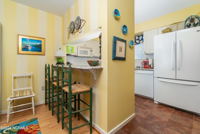 kitchen with white appliances, baseboards, a kitchen bar, light countertops, and white cabinetry