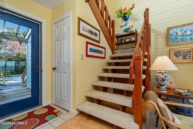 entrance foyer with baseboards, wood walls, stairs, and light tile patterned flooring