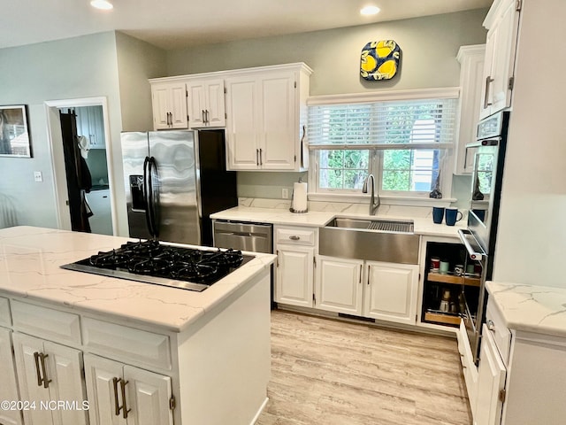 kitchen featuring a kitchen island, sink, light wood-type flooring, white cabinetry, and appliances with stainless steel finishes