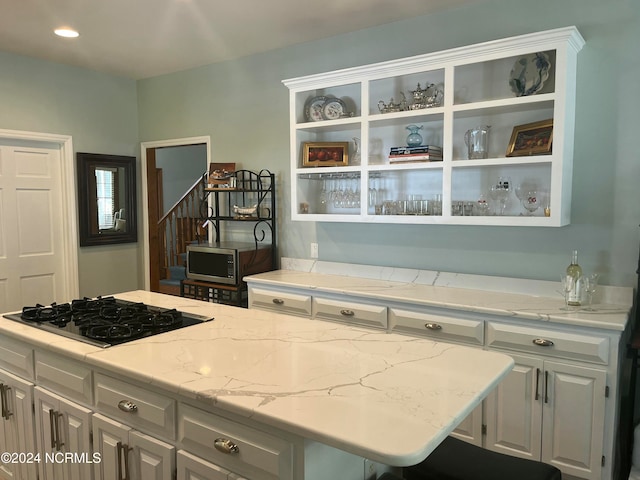 kitchen featuring light stone countertops, white cabinets, and black gas cooktop