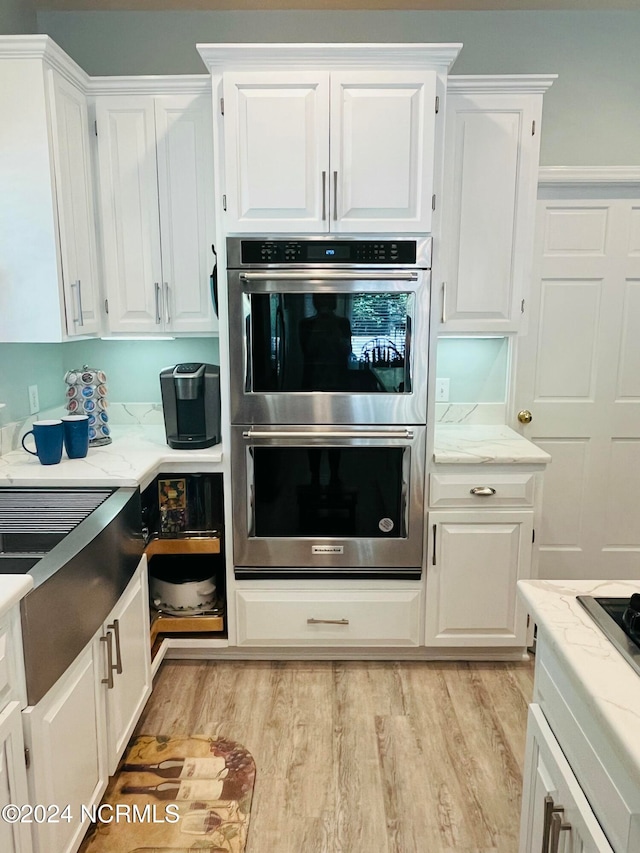 kitchen with white cabinets, light wood-type flooring, and stainless steel double oven