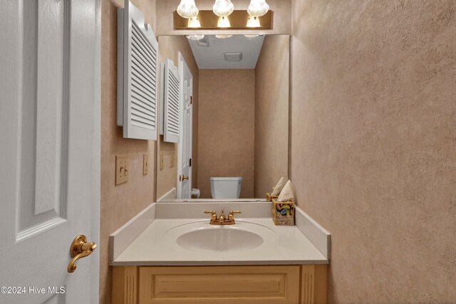 half bath featuring toilet, a textured wall, and vanity