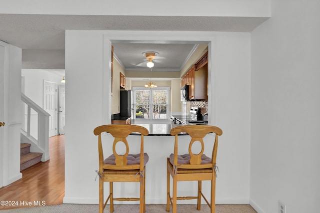 kitchen with light carpet, stainless steel appliances, ornamental molding, backsplash, and an inviting chandelier