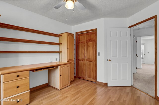 unfurnished office with a ceiling fan, built in study area, a textured ceiling, light wood-type flooring, and baseboards