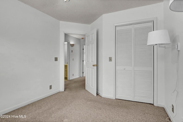 unfurnished bedroom with a textured ceiling, a closet, baseboards, and light colored carpet