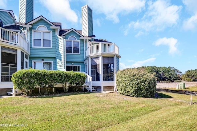 rear view of house featuring a yard, a chimney, and a balcony