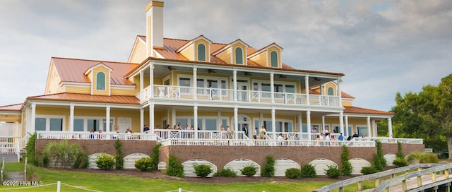 view of front of property featuring a balcony, a chimney, metal roof, a standing seam roof, and a front yard