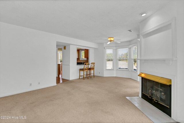 unfurnished living room with light carpet, ceiling fan, baseboards, and a tiled fireplace