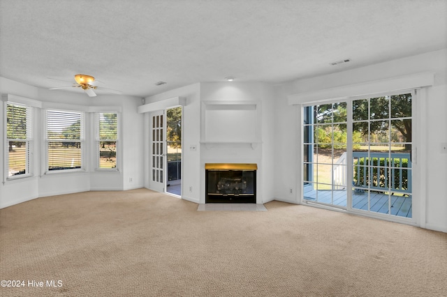 unfurnished living room with a fireplace with flush hearth, light carpet, a textured ceiling, and a ceiling fan