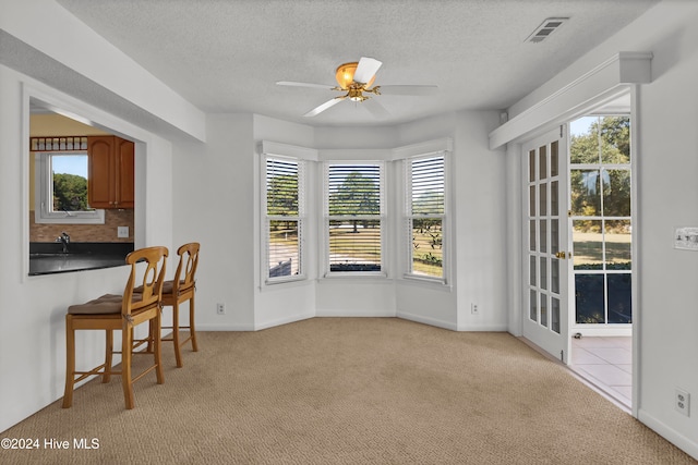 dining area featuring light colored carpet, visible vents, plenty of natural light, and a textured ceiling