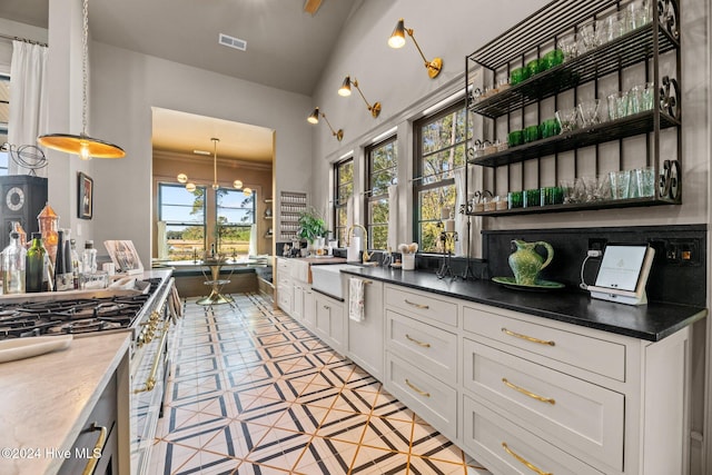 kitchen with decorative backsplash, high end stainless steel range oven, white cabinetry, pendant lighting, and sink