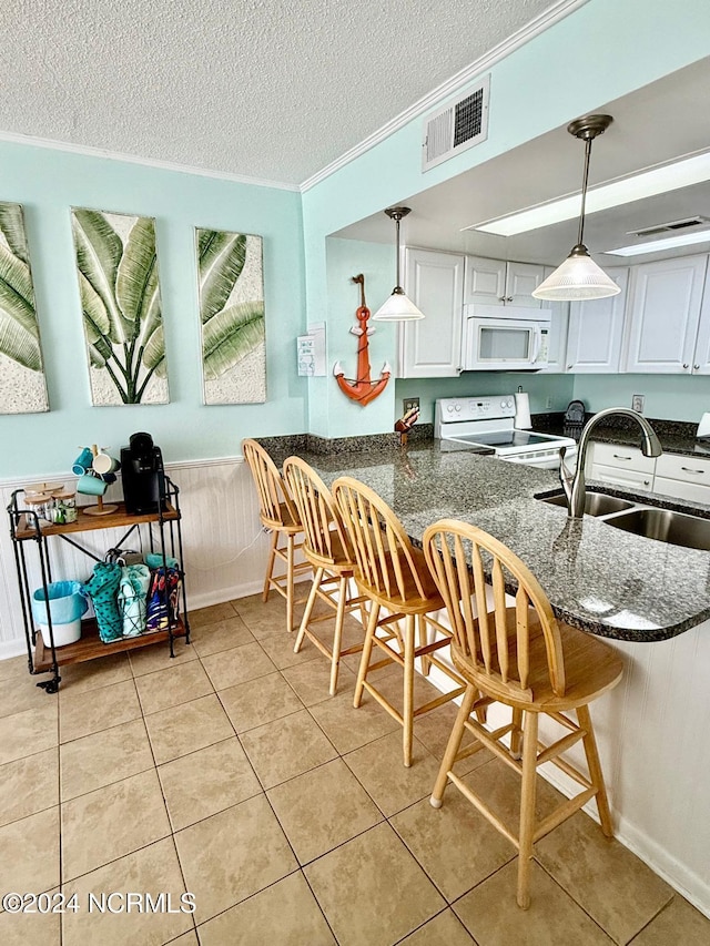 kitchen with white appliances, sink, white cabinetry, pendant lighting, and a breakfast bar