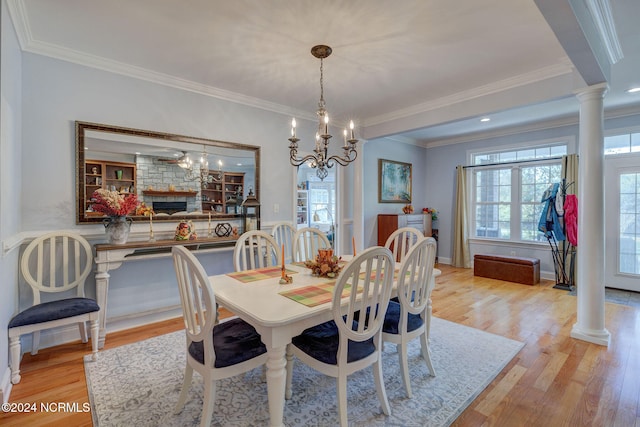 dining room with a fireplace, ornate columns, light hardwood / wood-style floors, crown molding, and an inviting chandelier