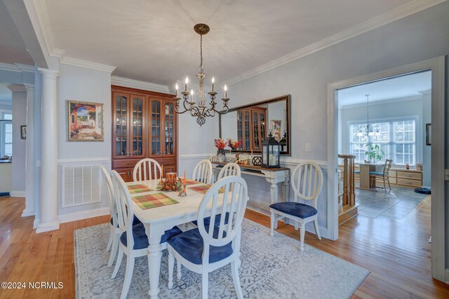 dining area featuring ornamental molding, a chandelier, light wood-type flooring, and decorative columns