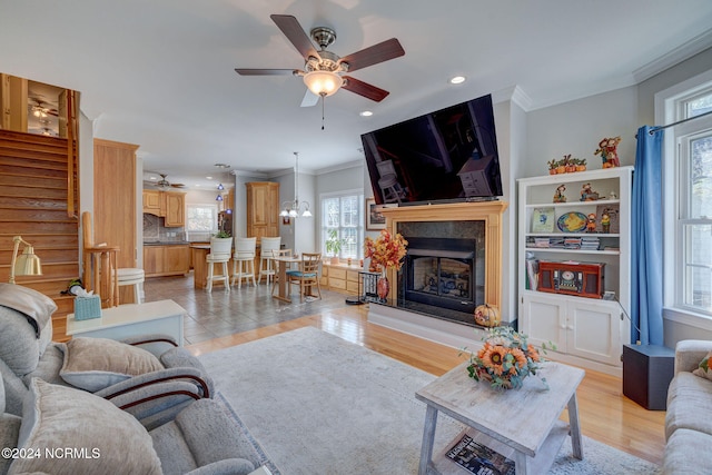 living room with light hardwood / wood-style floors, ornamental molding, and ceiling fan with notable chandelier