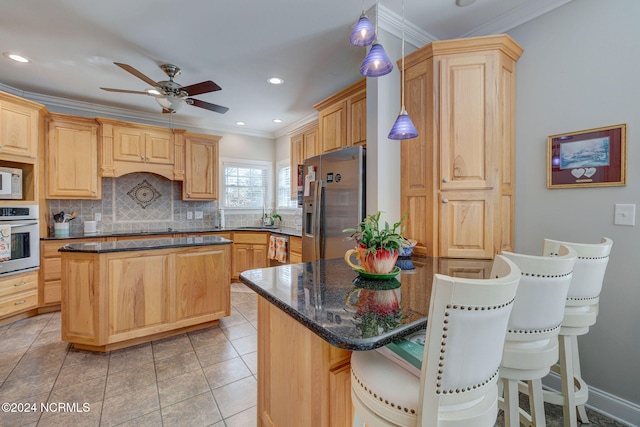 kitchen with stainless steel appliances, light brown cabinets, a kitchen island, and hanging light fixtures