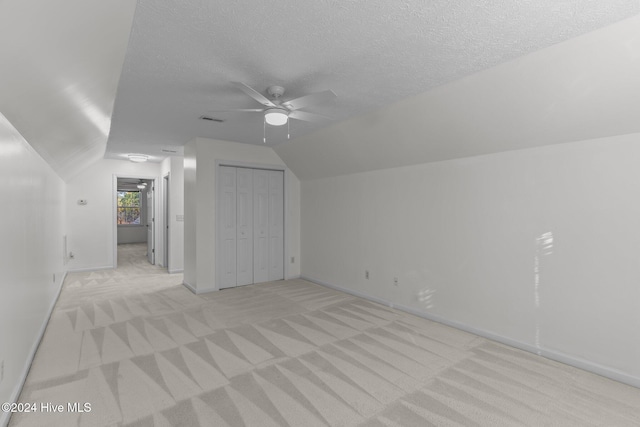 additional living space featuring a textured ceiling, ceiling fan, light carpet, and vaulted ceiling