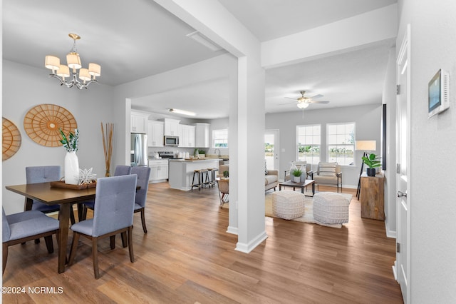 dining room with light hardwood / wood-style flooring and ceiling fan with notable chandelier